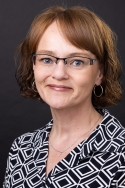 Woman wearing black and white top and glasses smiles serenely