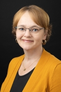 Woman wearing a mustard yellow cardigan sweater and glasses smiles serenely